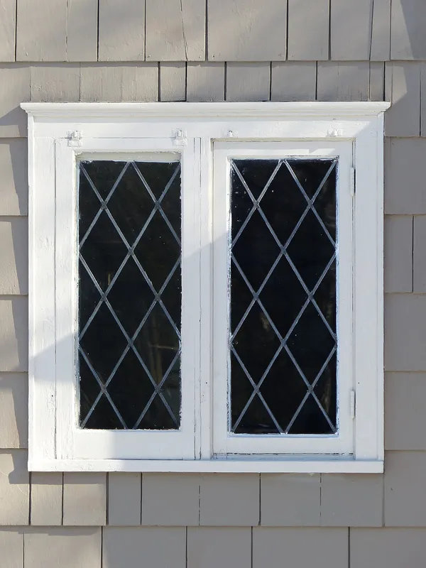 A pair of white casement sashes with leaded diamond glazing in a shingled wall