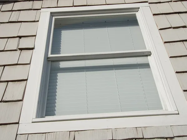 A double-hung window with the blinds down in a shingled wall