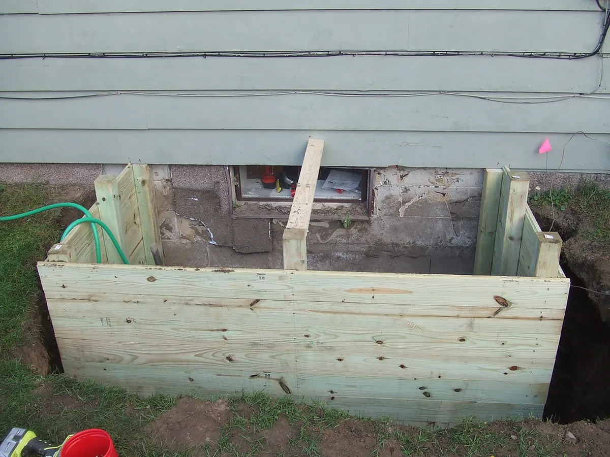 A timber window well built against a foundation wall below a basement egress window opening in a house like those in McDonough GA