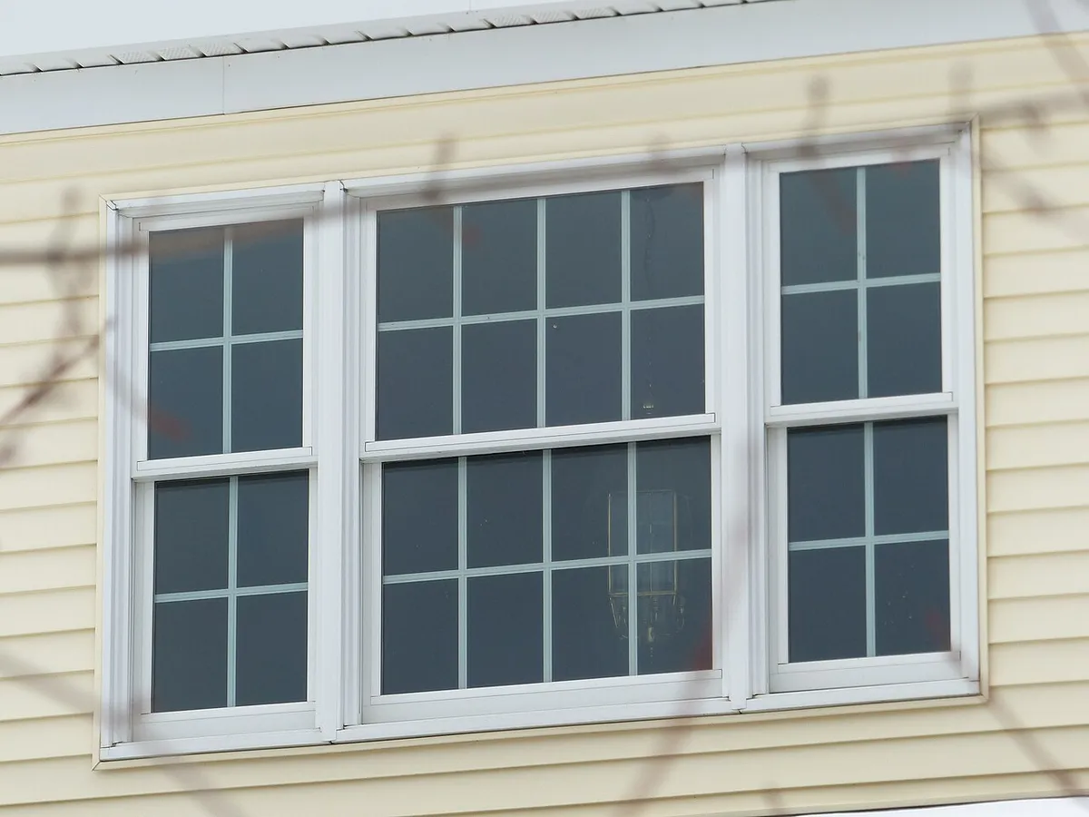 Three white double-hung windows side by side in a light vinyl-sided wall