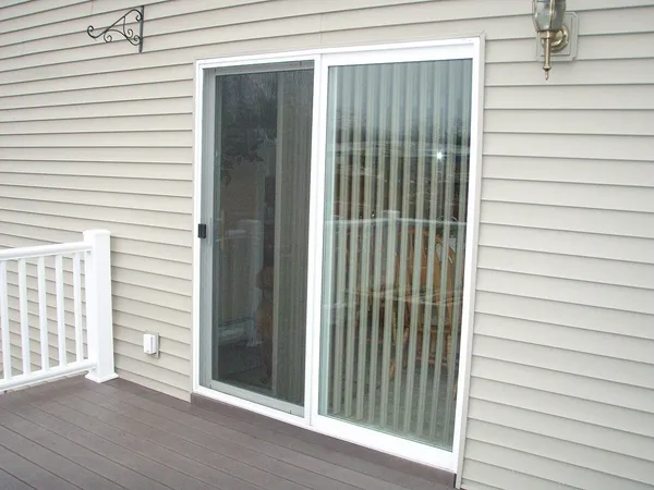 A white sliding patio door in a vinyl-sided wall, opening onto a deck