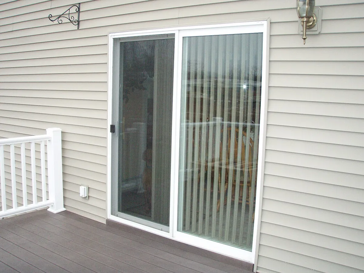 A white sliding patio door in a vinyl-sided wall opening onto a deck